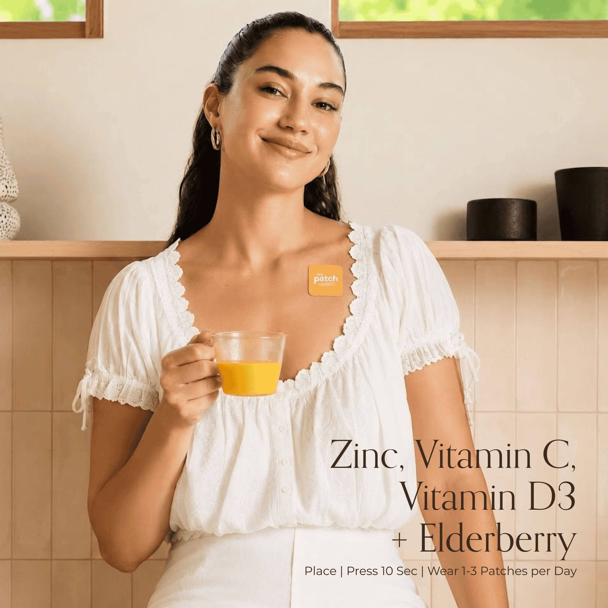 Woman at home holding a glass of orange juice with an Immunity patch on her chest, next to the text Zinc, Vitamin C, Vitamin D3 + Elderberry and usage instructions Place, Press 10 Sec, Wear 1-3 Patches per Day