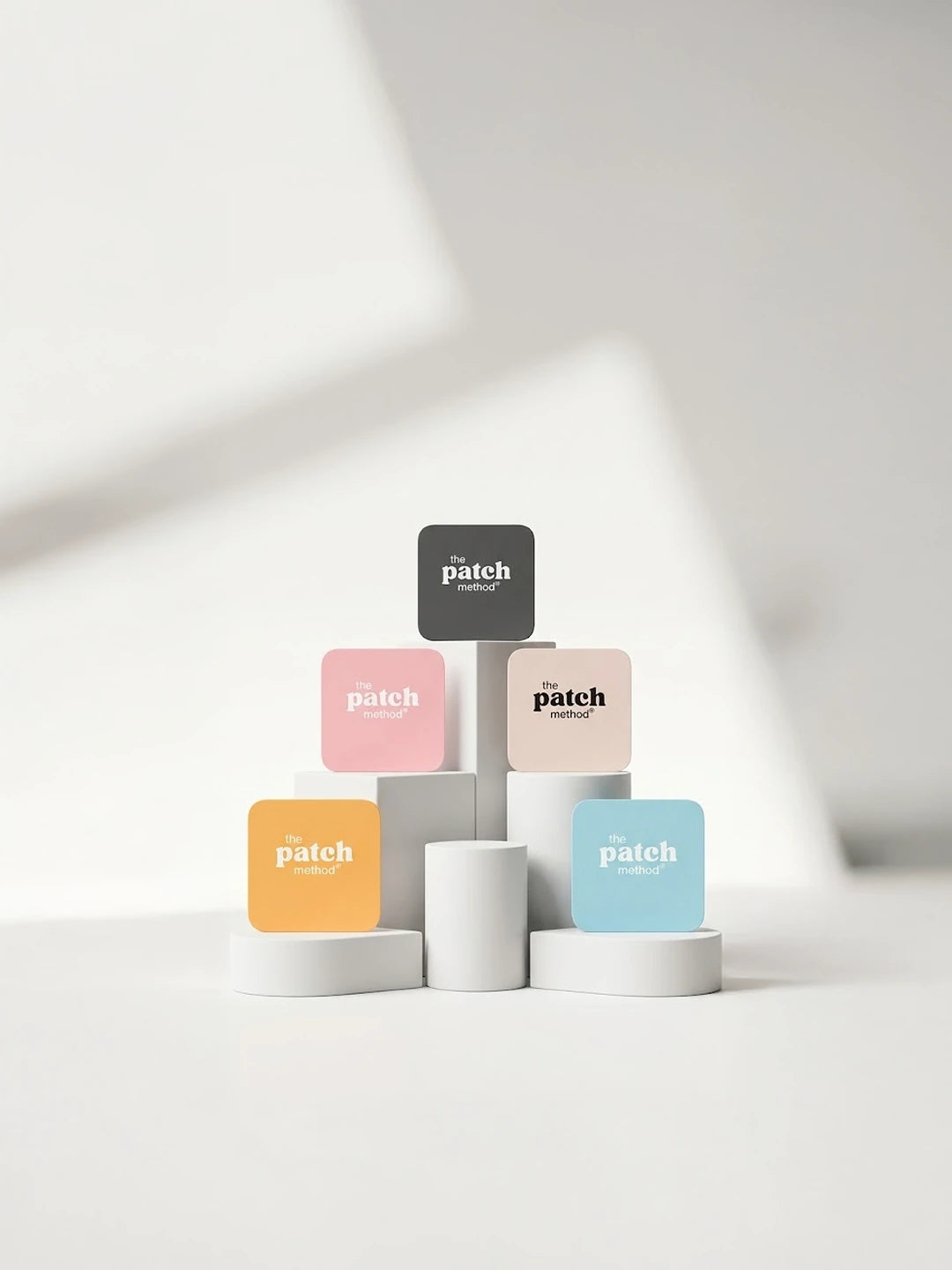 Five colored Patch Method patch tiles (charcoal, pink, tan, orange, and light blue) arranged on white geometric pedestals, cropped for mobile with empty space at right